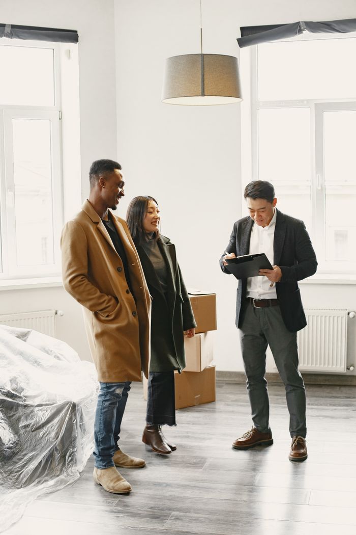 Three adults in a modern apartment discussing real estate, with moving boxes in the background.