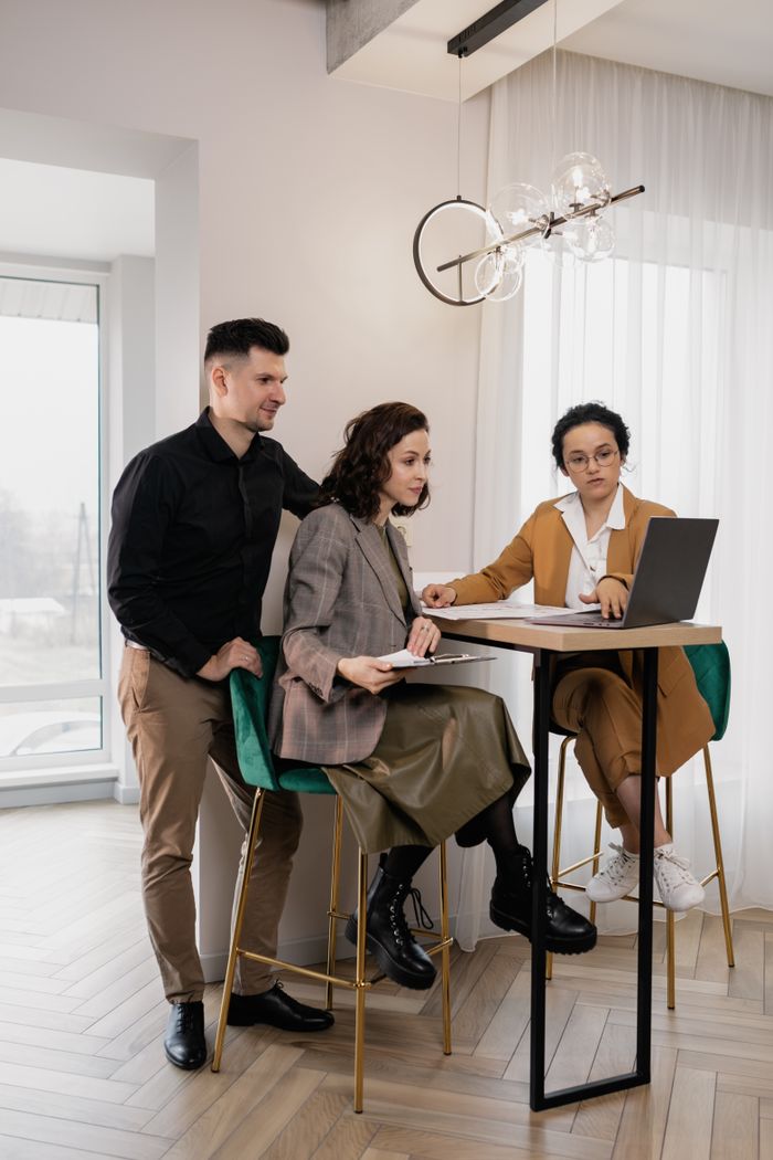 Three young professionals collaborating at a high table, focused on a laptop.